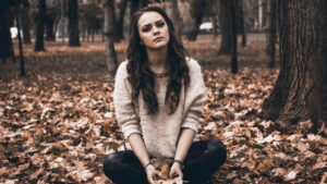 Image of woman in a sweater sitting on the ground covered with leaves